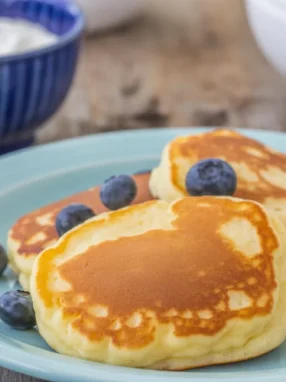 Fluffy Oladi pancakes topped with fresh berries and sour cream, served for breakfast.