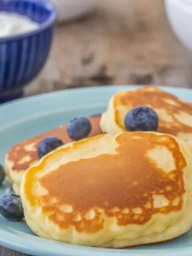 Fluffy Oladi pancakes topped with fresh berries and sour cream, served for breakfast.