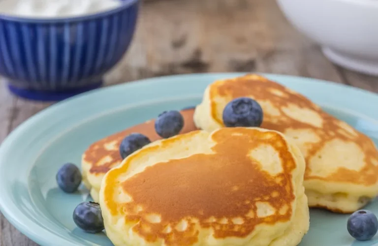 Fluffy Oladi pancakes topped with fresh berries and sour cream, served for breakfast.