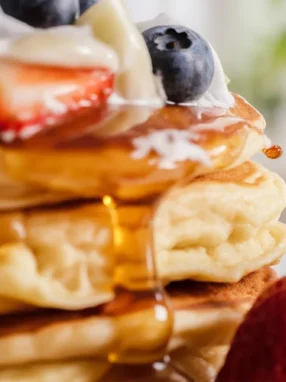 Delicious fluffy KEFIR PANCAKES stacked on a plate with syrup and berries