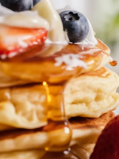 Delicious fluffy KEFIR PANCAKES stacked on a plate with syrup and berries