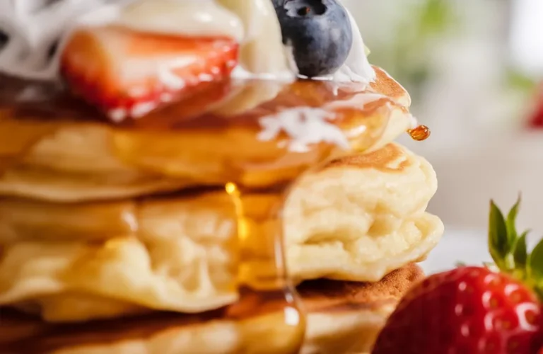 Delicious fluffy KEFIR PANCAKES stacked on a plate with syrup and berries